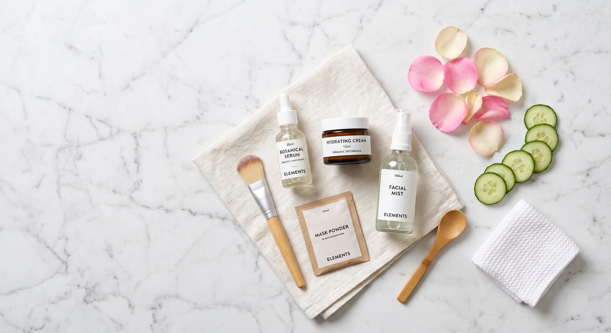 Hochwertige Naturkosmetikprodukte, Cremes, Gurkenscheiben und Rosenblüten stilvoll arrangiert auf einer hellen Marmorplatte im Badezimmer.